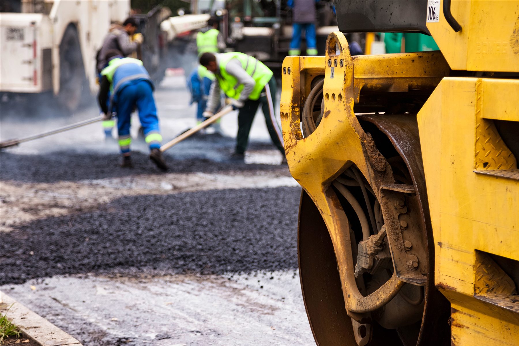 Road construction crew working beside heavy paving machinery